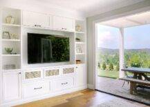 White built-in TV cabinets accented with oil rubbed bronze hardware and positioned beneath an above a flat panel television flanked by styled white shelves.