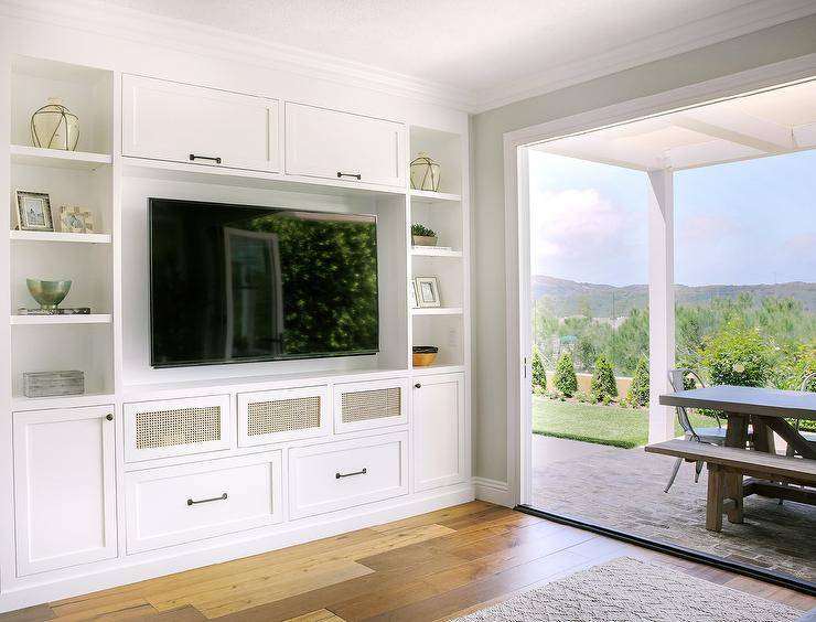 White built-in TV cabinets accented with oil rubbed bronze hardware and positioned beneath an above a flat panel television flanked by styled white shelves.