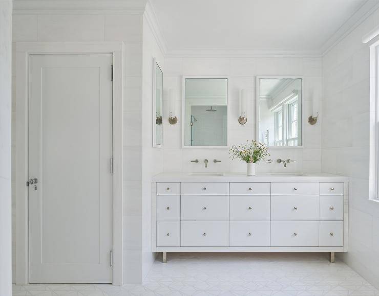 Spacious bathroom features a modern white double washstand under white Parsons mirrors flanked by long sconces.