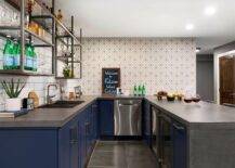 Kitchen features a blue U-shaped wet bar with concrete countertops, gray geomeric tiles backsplash, stainless steel industrial shelves on white offset tiles and large gray floor tiles.