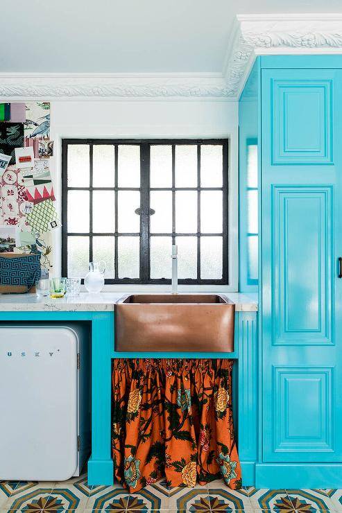 Eclectic blue kitchen features a copper farm sink with orange skirt and blue cabinets.