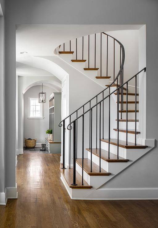 Curved staircase with wrought iron handrails and spindles featuring stained wood stair treads complementing stained wood floors.