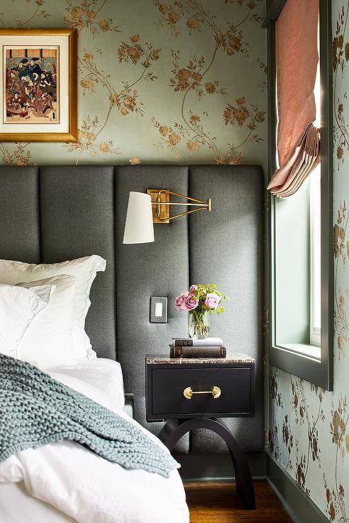 White and gold swing arm sconces on a blue art deco channel-tufted headboard in an eclectic bedroom design. A black nightstand with a black marble top pairs together with the bed and wall to wall headboard.