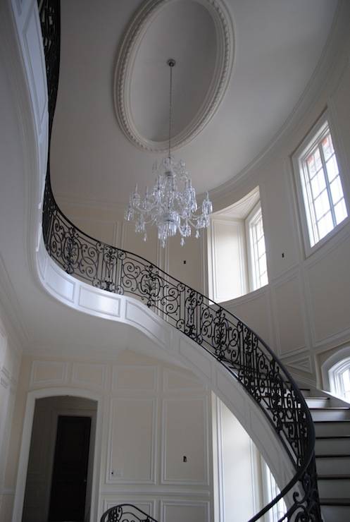 Serambi 2 lantai yang menakjubkan dengan tangga berkelok-kelok, pagar tangga besi, dan lampu kristal.