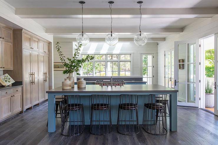 Brown and blue kitchen features a blue center island lit by three glass lanterns hung over a concrete countertop finished with a sink.