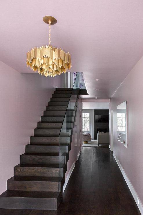 Desain serambi bercat merah muda menampilkan lampu gantung logam emas di atas tangga bernoda gelap dengan pagar kaca.