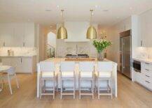 A custom lighted kitchen island is complemented with white and beige counter stools and gold dome pendants hung on either side of a polished nickel faucet.