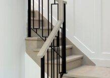 A gray wash wood staircase is finished with hollow iron balusters alongside a staircase wall clad in wainscoting.