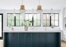Two Kelly Wearstler Precision Pendants illuminate a peacock blue kitchen island finished with a sink and a brass gooseneck faucet.