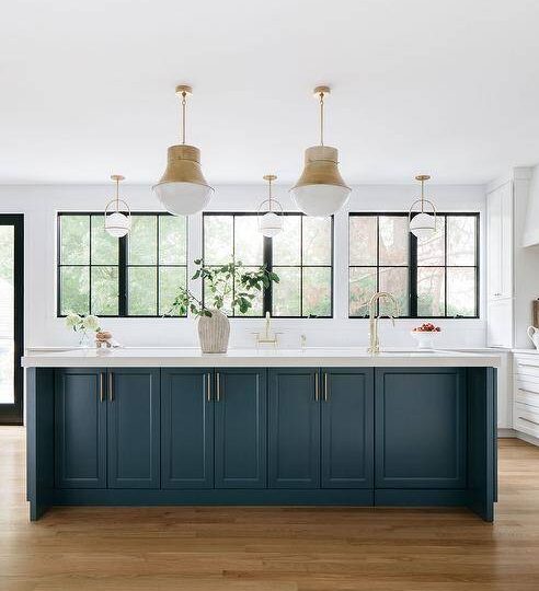 Two Kelly Wearstler Precision Pendants illuminate a peacock blue kitchen island finished with a sink and a brass gooseneck faucet.