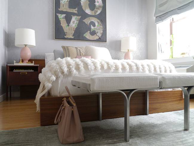 Fantastic bedroom with love art over wood platform bed dressed with Moroccan wedding blanket with wide headboard flanked by pink lamps on mid-century modern nightstands as well as mid-century modern bench at foot of bed over gray rug.