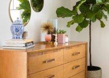 Warm toned mid-century modern dresser in a bedroom balanced by a white wall featuring three staggered round mirrors. A fiddle leaf fig plant decorates the space with color and an organic vibe along with decorative pieces on the modern dresser.