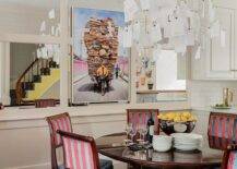 Paper notes chandelier illuminates a French dining table fitted with red and blue French chairs in an eclectic dining room design.