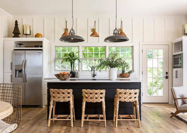 Charming cottage kitchen features basketweave counter stools placed at a black shiplap kitchen island illuminated by industrial lanterns.