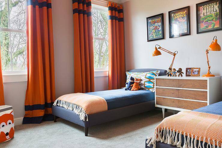 Alyssa Rosenheck - Emily Lister Interiors - Blue and orange shared boys' bedroom features framed comic book covers placed over a pair of blue linen upholstered twin beds dressed in blue bedding and an orange herringbone throw flanking a shared mid century modern dresser as nightstand topped with orange task lamps placed next to windows dressed in bright orange curtains with blue stripes.