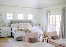 Stylish pink and gray contemporary bedroom boasts a lounge area featuring pink chaise lounges topped with white sheepskin throws and pink and brown pillows. The chaise lounges sit on a metallic cowhide rug beneath a brass chandelier.