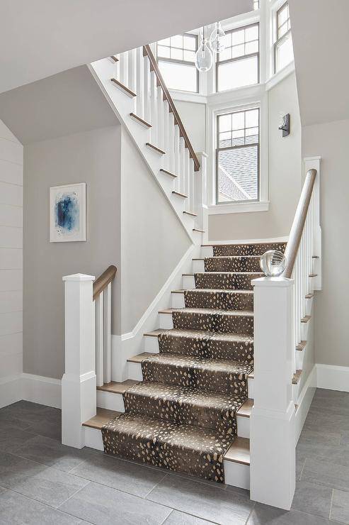 A white staircase post is fitted with a crystal ball fixed in front of a brown stained wood handrail accenting white wooden spindles, while an antelope print runner covers brown stained wood treads.