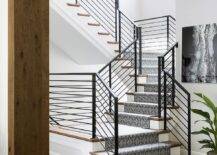 A gray geometric staircase runner covers stained wood treads and accents a staircase finished with an iron handrail.