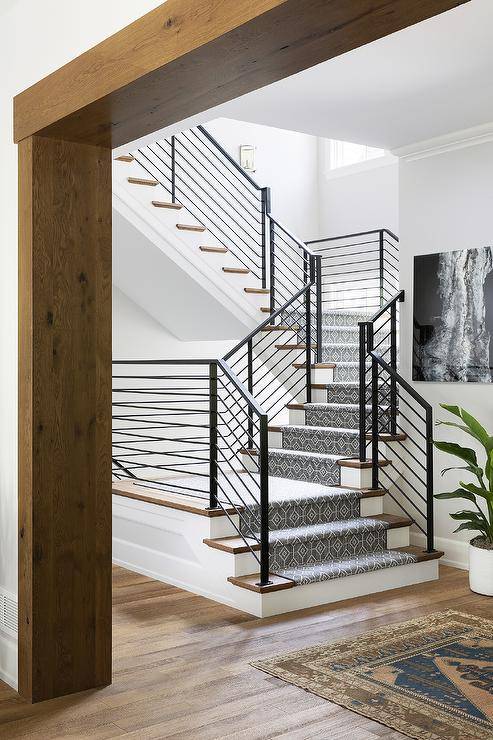 A gray geometric staircase runner covers stained wood treads and accents a staircase finished with an iron handrail.