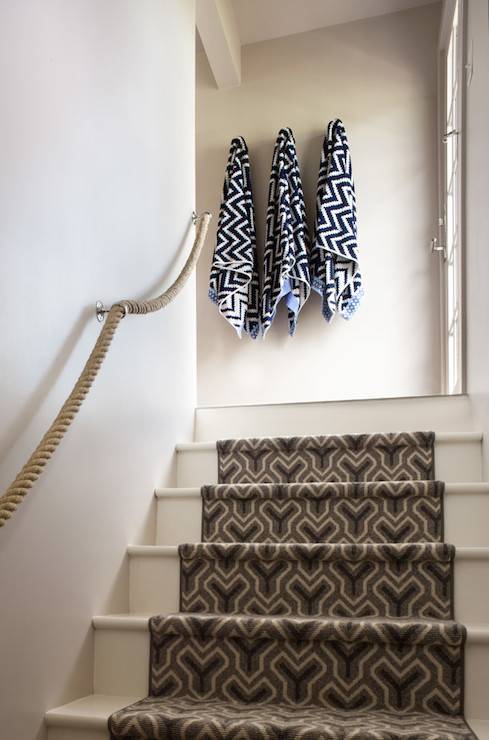 Cottage home features stairwell with rope railing and steps covered in gray and black geometric stair runner as well as towel hooks located at the top of the stairs.