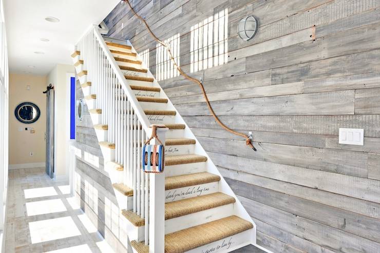 Seaside cottage foyer features staircase with sisal steps and rope railing on wood planked wall.