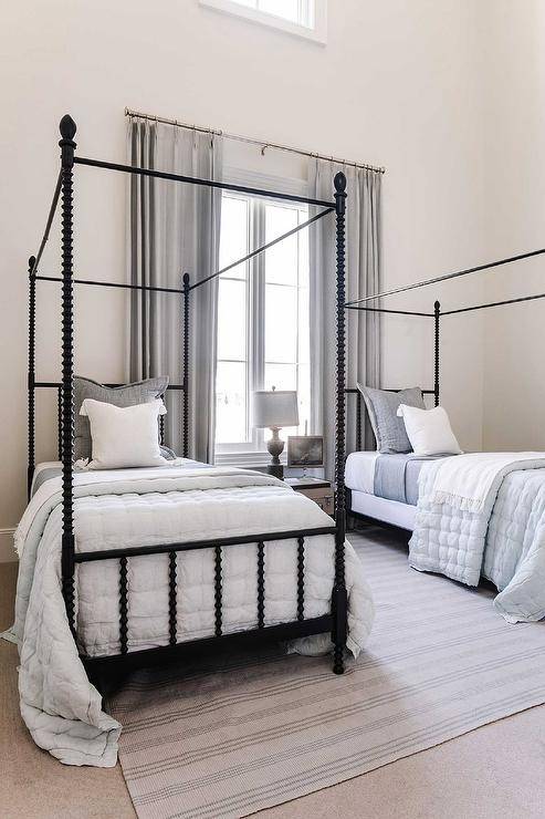 Boys room features black spindle canopy beds with gray and blue bedding on a gray strip rug and a black marble urn lamp that illuminates a vintage trunk as a shared bedside table.