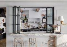 Kitchen passthrough with black folding doors, marble bar and brass and lucite round back barstools are featured in this transitional dining room.