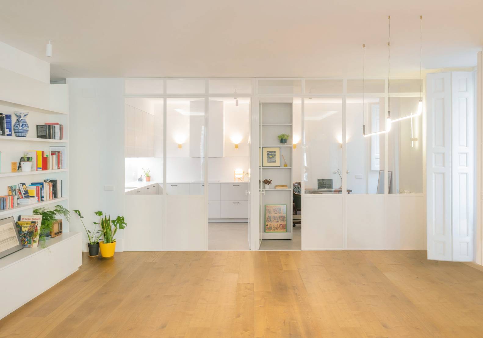 open concept living room with bookshelves lining left side, wall of windows and warm wood floors