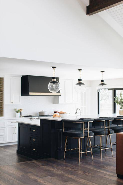 Black velvet stools at a black island with a breakfast bar topped with white quartz in a transitional kitchen. A set of glass and black globe pendant lights align above the island and raised breakfast bar design.
