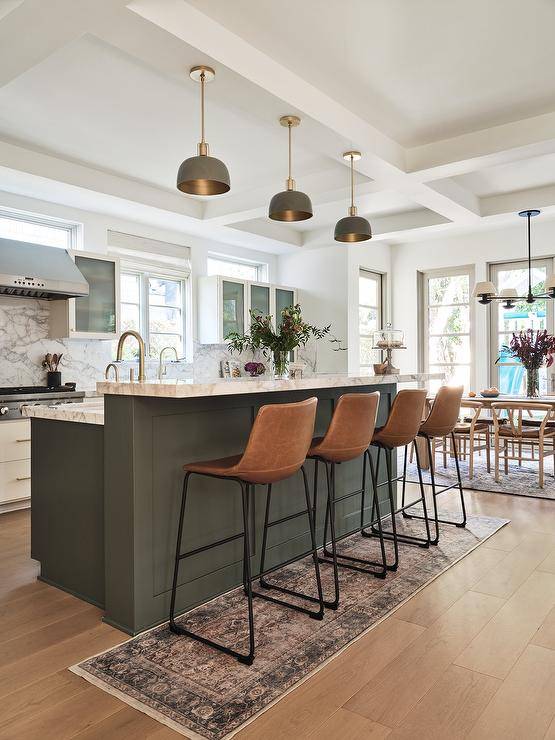 Kitchen features brown molded leather stools atop a vintage runner at a Forest Green island with marble top lit by gold and green pendants.