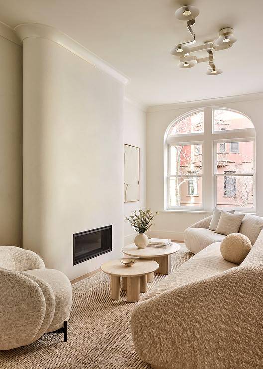 Monochromatic living room with modern fireplace features a cream modular sofa with round oak coffee tables and cream accent chair.