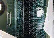 Shower boasts green herringbone pattern walls, clear shower doors and black hexagon floor tiles.