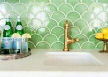 A smalled curved sink with a brass faucet completes a wet bar accented with green fan-shaped tiles.