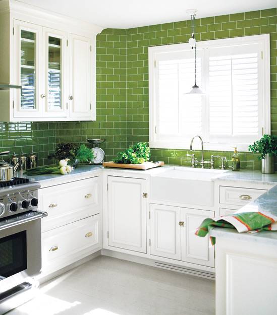White and green kitchen with crisp white cabinets paired with carrara marble countertops and green subway tile backsplash. Vintage barn pendant light hangs over farmhouse sink with polished nickel bridge faucet. U shaped kitchen features stainless steel appliances and green leafy accents.