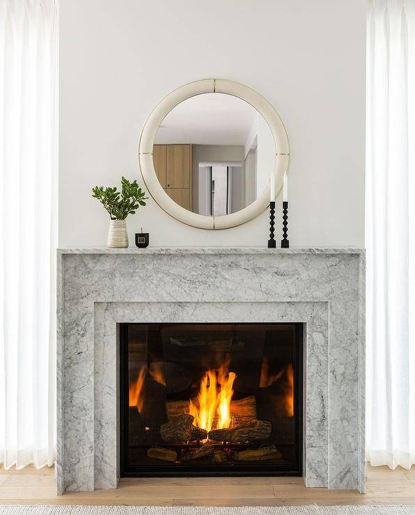 Bedroom features a round ivory shagreen mirror over a marble fireplace mantel.
