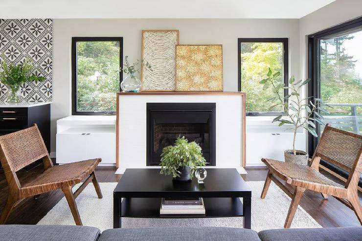 Mid century modern fireplace styled with two framed wall art pieces in a living room flanked by black framed windows and white built-in cabinets. A black coffee table furnishes the living space along with mid century modern chairs.