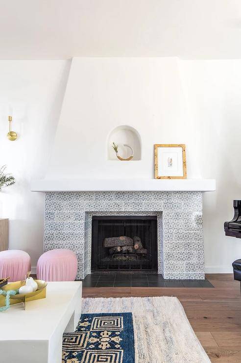 Pink stools sit in front of a vintage white and gray mosaic tiled fireplace positioned beneath a small arched niche.