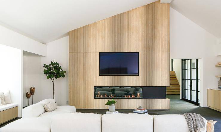 Living room features a tan reeded fireplace wall with a modern gas fireplace and flat screen TV and a modern ivory sectional.