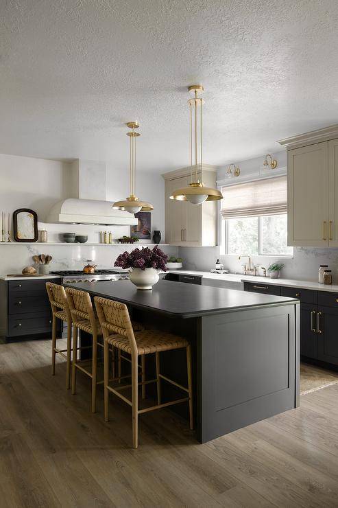 A black kitchen island with a black countertop is complemented with beige basketweave stools and lit by two brass vintage lanterns.