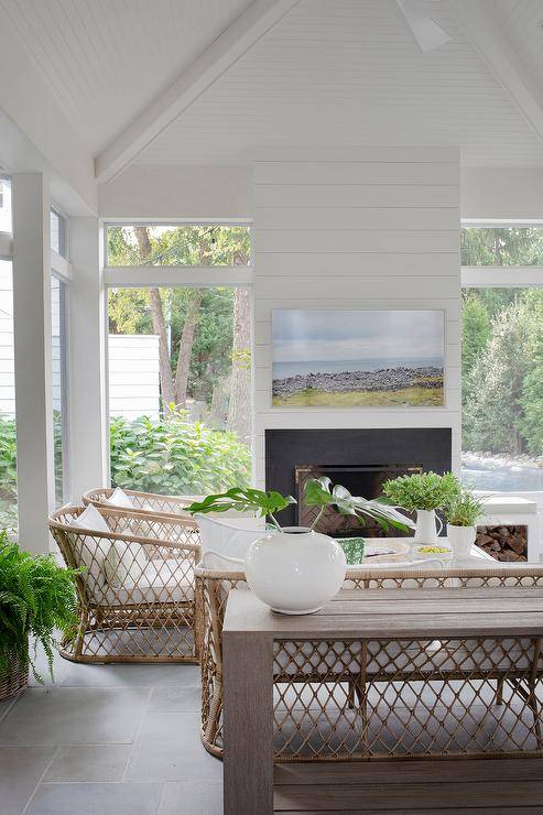 Cottage style sunroom features light brown rope and rattan accent chairs and a light brown rope and rattan sofa atop a gray slate floor and a white shiplap fireplace wall.