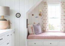 Girls bedroom reading nook alcove finished with a bench and pink cushion. Vertical shiplap walls bring a cottage look to the walls along with a white wood dresser accebtednwith oil rubbed bronze hardware.