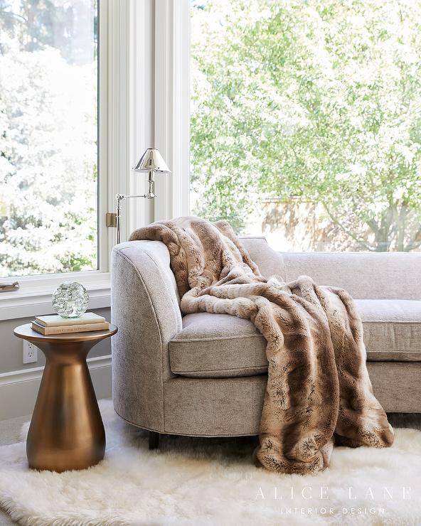Bedroom bay window boasts a taupe brown curved sofa with a gold accent table on a white sheepskin rug.