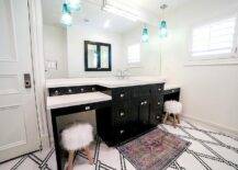 Chic black and white contemporary kids' bathroom features a black and pink rug placed on black and white penny floor tiles in front of a black washstand accented with polished nickel hardware and a white quartz countertop. The sink, paired with a polished nickel hook and spout faucet, is flanked by drop down makeup vanities seating round sheepskin stools. A frameless vanity mirror is lit by turquoise blue glass pendant lights and a box sconce mounted on it.
