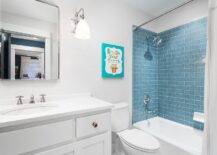 White and blue kid's bathroom boasts drop-in bathtub accented with blue subway wall tiles and a polished nickel shower head and tub filler. A white and gray shower curtain hangs in front of the bathtub, as a kids' canvas art piece is positioned over a toilet. CompPimlico Swing-Arm Sconces flank a curved nickel vanity mirror and illuminate a white bath vanity finished with polished nickel knobs and a round sink with a polished nickel faucet kit.