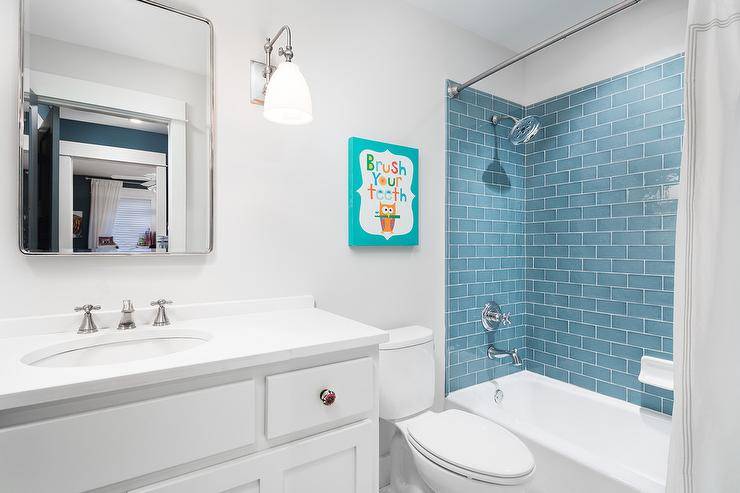 White and blue kid's bathroom with blue subway wall tiles and a polished nickel shower faucet over white tub