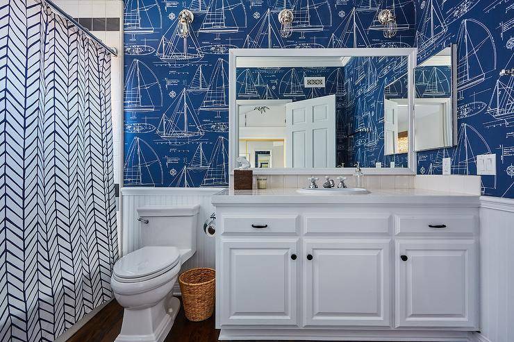 Navy nautical boat themed wallpaper in child's bathroom with white vanity cabinets and navy geometric shower curtain