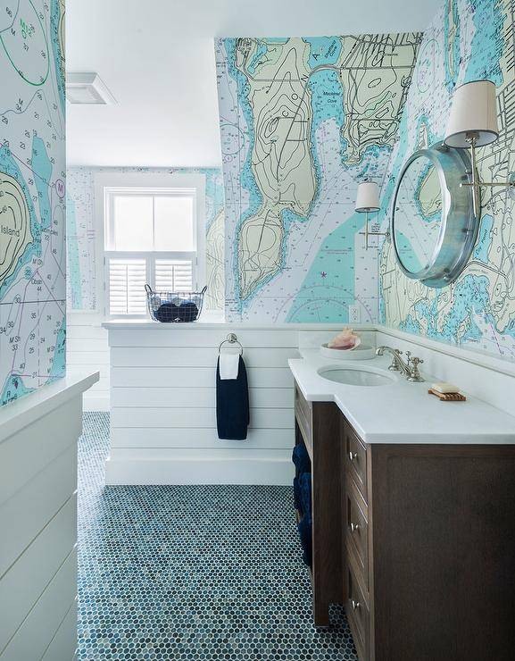 kids cottage bathroom with a white quartz countertop beneath porthole mirror mounted on geographical world map wallpaper accented with a shiplap trim as blue hexagon floor tiles cover the floor