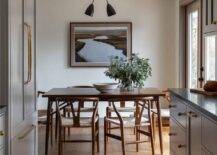 A landscape art piece hangs behind a mid-century modern dining table accented with brown wishbone dining chairs.