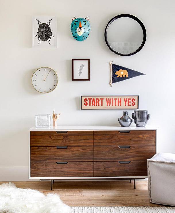 An art gallery is displayed over a two tone mid century modern nursery dresser.