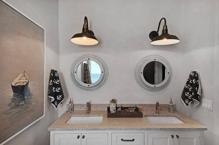 boy's nautical bathroom with two large black vintage wall sconces mounted on gray walls over porthole mirrors fixed above a white dual vanity
